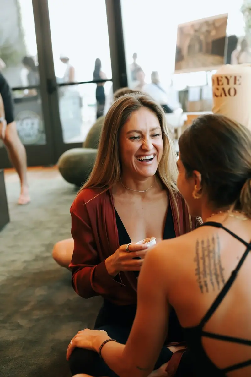 Two women laughing together on the floor at a Welda gathering