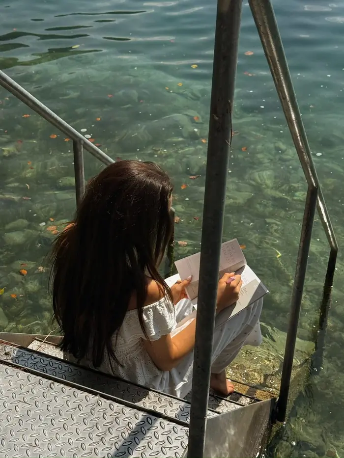 A woman journaling on the steps down to clear water