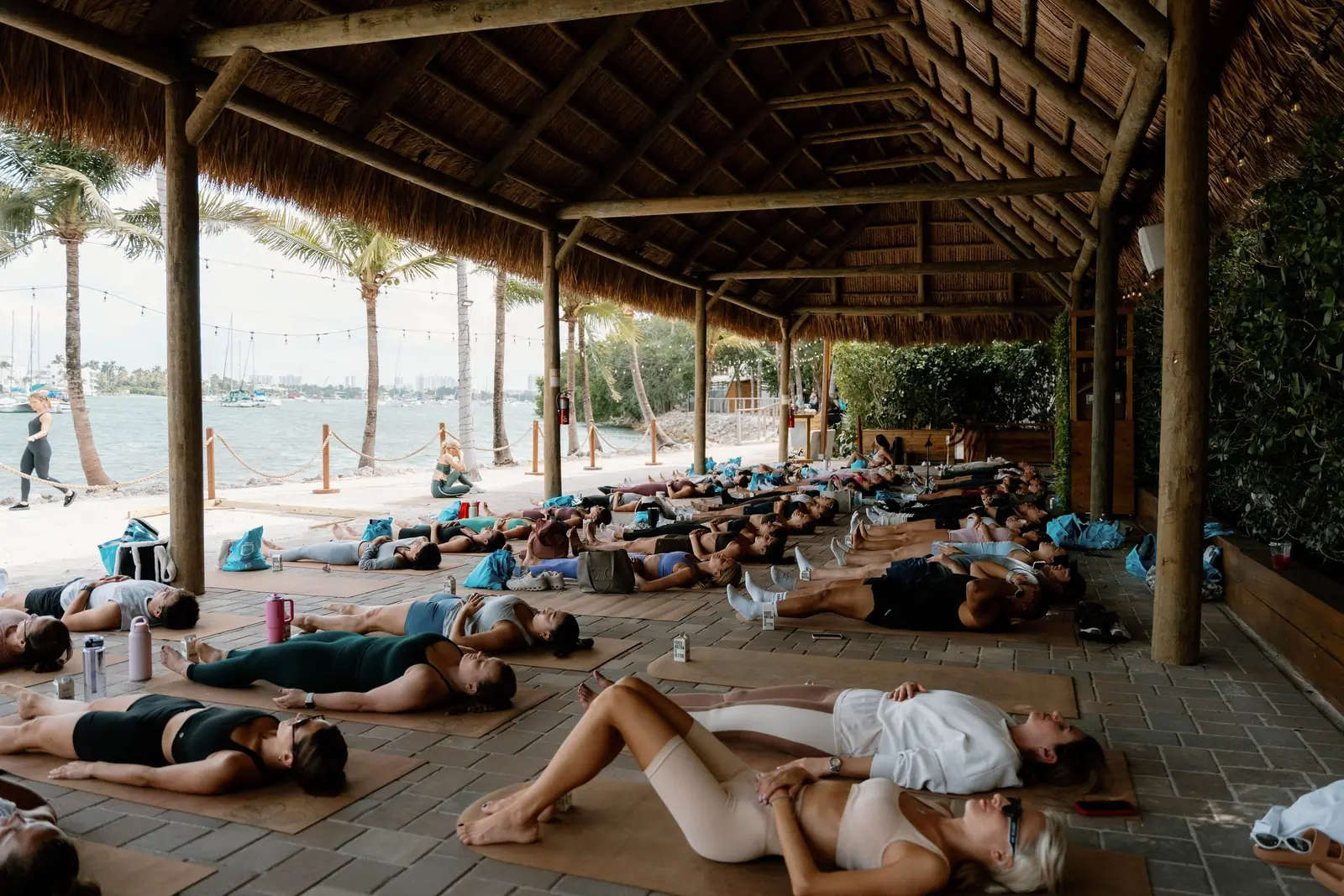 A group resting on mats in savasana under a thatched beachfront pavilion in South Florida