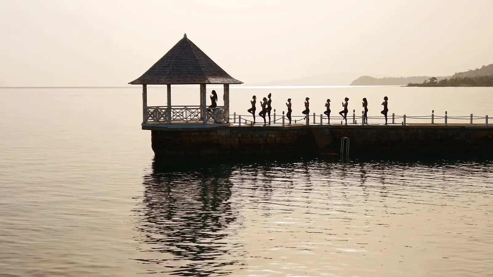 Guests holding tree pose along a seaside pier at dusk in Jamaica