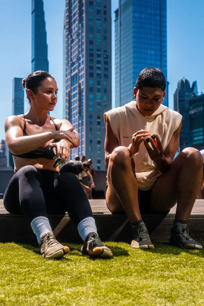 Two people resting on the grass after a workout, with skyscrapers behind them