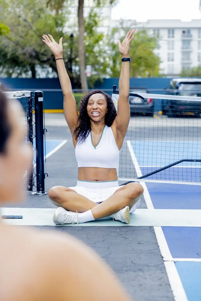 A woman cheering with her arms raised, sitting cross-legged on a court