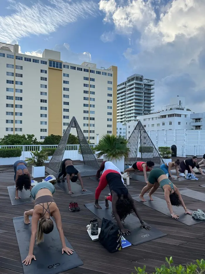 A rooftop yoga class holding downward dog, with Miami Beach buildings behind